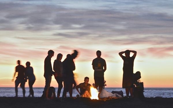 Jóvenes en grupo en torno a un fuego en la playa al atardecer